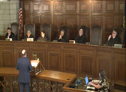 Justice Jonathan Papik, Justice Stephanie Stacy, Justice Lindsey Miller-Lerman, Chief Justice Mike Heavican, Justice William Cassel, Justice John Freudenberg with Justice Jeff Funke participating via video conferencing. Arguing before the Court is Attorney Alton E. Mitchell. Recording Court arguments is Allyson Stewart.